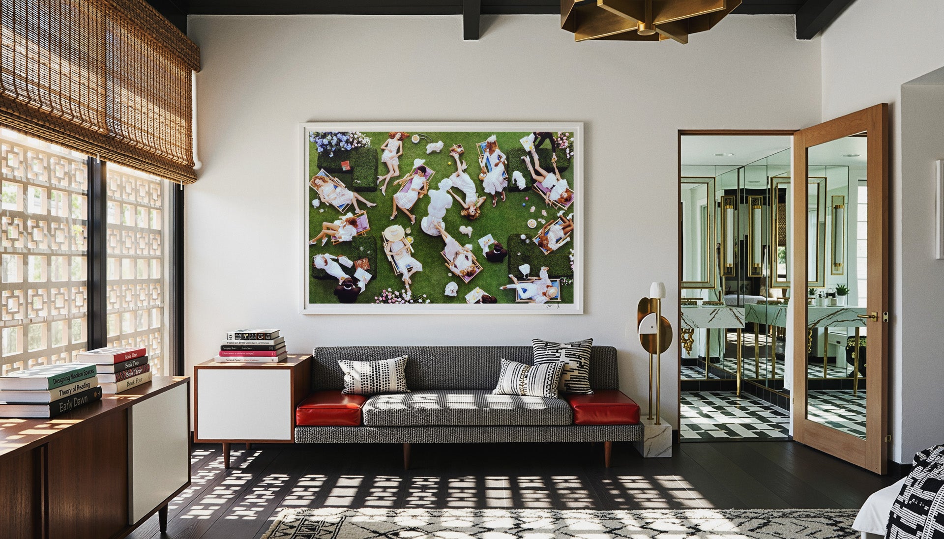 In situ record of Blossoming by Sebastian Mader, originally lensed for Vogue Japan (2018). This large-scale Studio Edition, an aerial garden tableau with subjects in white attire, is displayed in a mid-century modern Palm Springs living room. The record documents the graphic interplay of light and shadow cast by a lattice screen across a modernist sofa and black wood floors, with a checkered-floor bathroom visible through a timber doorway. Materiality: Archival pigment on Hahnemühle Fine Art Baryta
