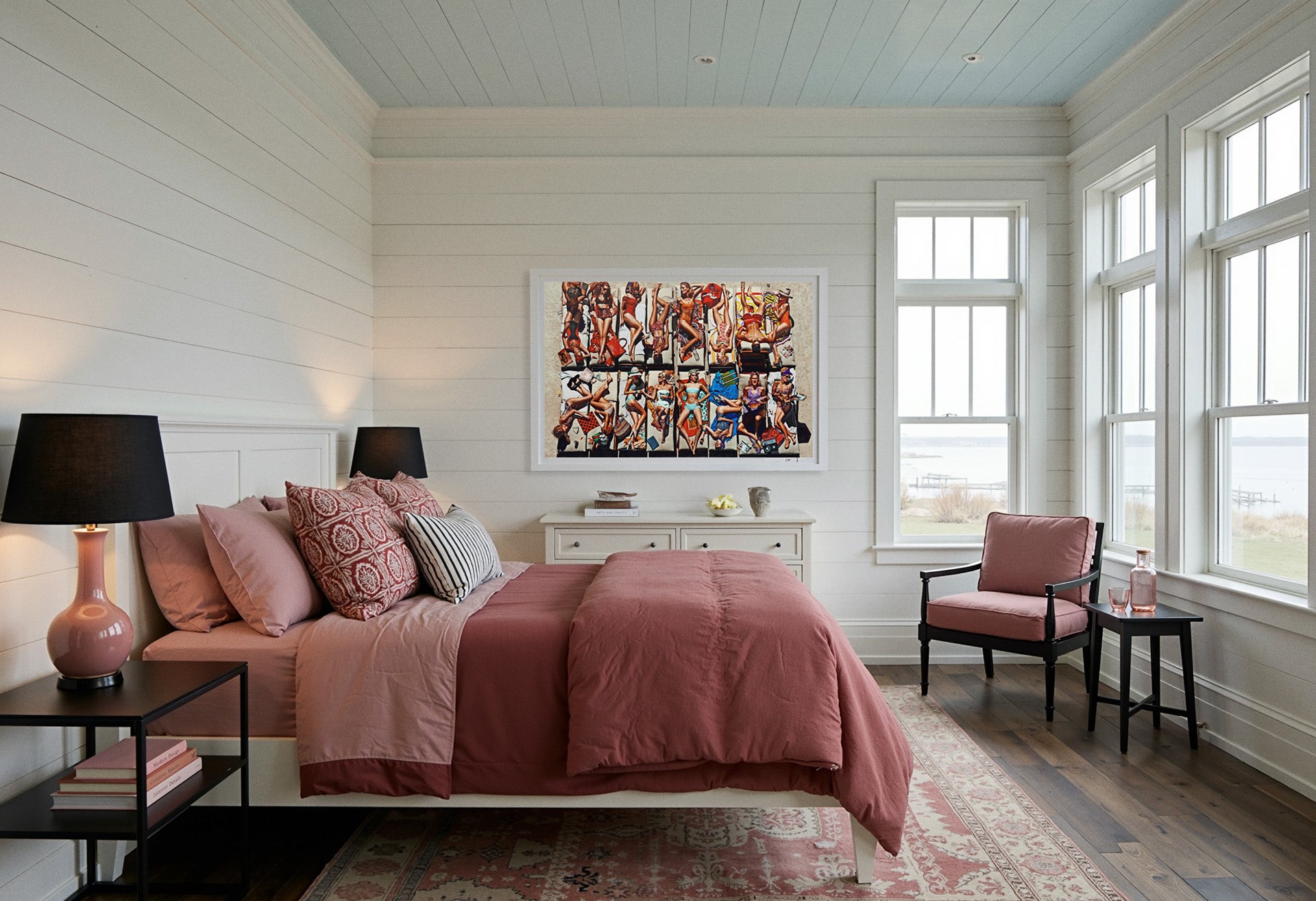 Sebastian Mader | Flamingo Kids #2 | Studio Edition. Archival record documenting the work installed in a light, coastal-inspired bedroom featuring white horizontal shiplap walls and a light blue painted plank ceiling. The composition, framed in satin white, is positioned above a dresser, contrasting with dusty rose bedding and windows overlooking a hazy water view. Materiality: Archival pigment on Hahnemühle Fine Art Baryta.